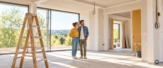 Paar steht in einem teilweise renovierten Wohnraum und betrachtet gemeinsam die geplanten Modernisierungsarbeiten.