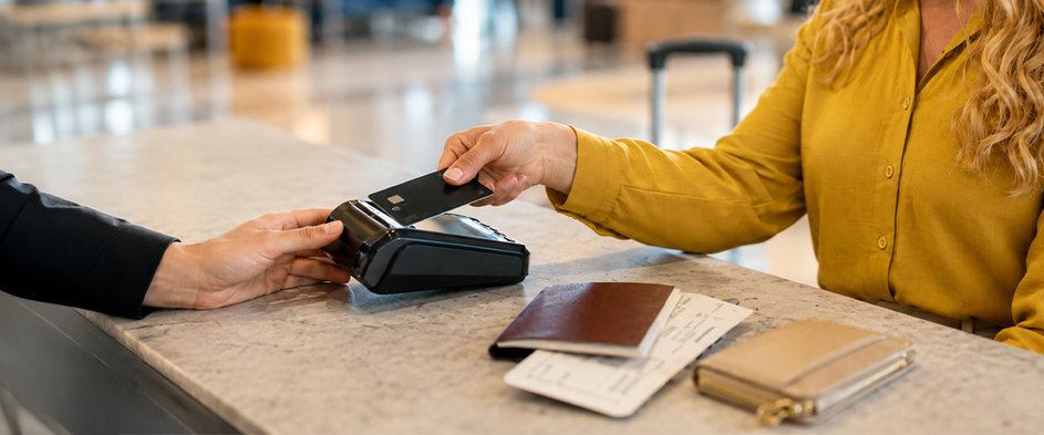 Eine Reisende bezahlt an einem Kartenterminal mit ihrer Bankkarte, daneben liegen Reisepass und Bordkarten – Symbolbild für das Bezahlen im Urlaub mit Karte und die Wahl des passenden Zahlungsmittels auf Reisen.