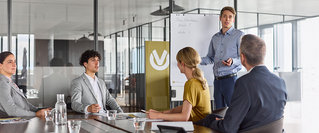 Mehrere Personen sitzen in einem modernen Besprechungsraum, während ein junger Mann eine Präsentation hält – Symbolbild für berufliche Neuorientierung, Karrierechancen und Weiterbildung beim Jobwechsel.