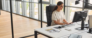 Eine Frau arbeitet an einem Schreibtisch im modernen Büro am Computer – Symbolbild für einen flexiblen Nebenjob mit Perspektive, freier Zeiteinteilung und unterstützender Tätigkeit zum Beispiel im Finanzbereich.
