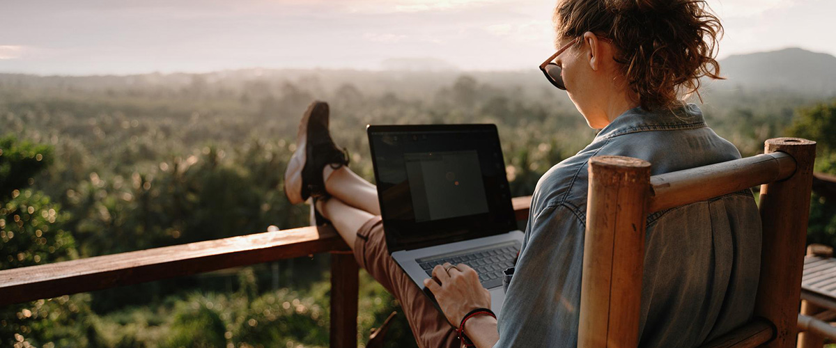 Young business woman working at the computer in cafe on the rock. Young girl downshifter working at a laptop at sunset or sunrise on the top of the mountain to the sea, working day.