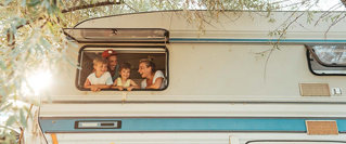 Fröhliche Familie im Wohnmobil beim Camping – sorglos unterwegs dank der richtigen Reiseversicherung 