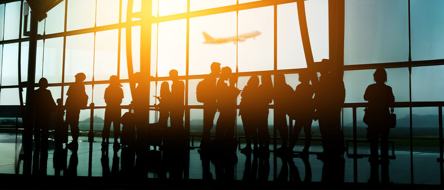 Reisende warten in der Abflughalle eines Flughafens vor großen Fensterfronten, während im Hintergrund ein Flugzeug startet – Symbolbild für Flugreisen sowie Fluggastrechte bei Verspätungen, Annullierungen und anderen Reiseunterbrechungen.
