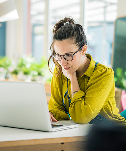 Frau mit grünem Oberteil, Zopf und Brille am Laptop
